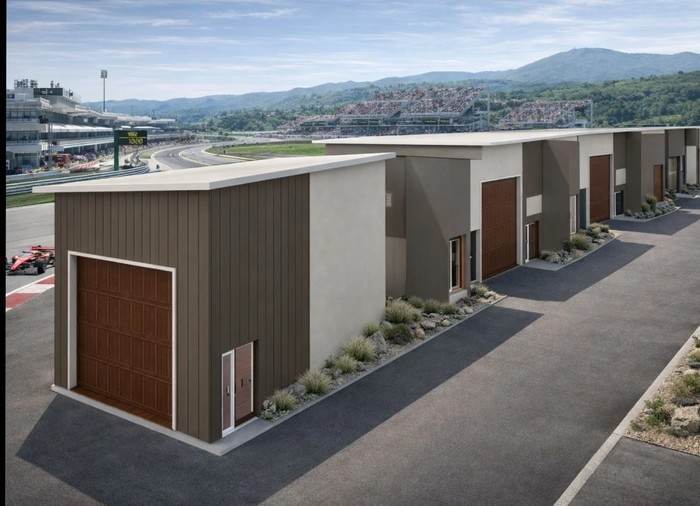 Luxury trackside car loft with open industrial garage bay beside a private motorsport circuit